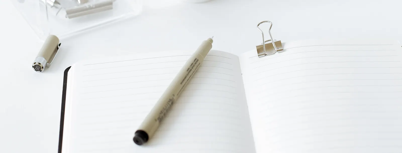 An open lined notebook with a pen and a metal clip on a white desk